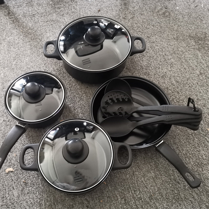 Set of black cookware with lids and utensils on a gray surface