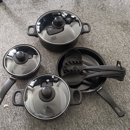 Set of black cookware with lids and utensils on a gray surface