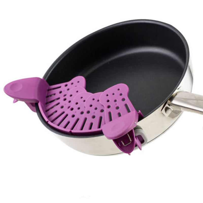 Purple silicone strainer clip on a frying pan against a white background