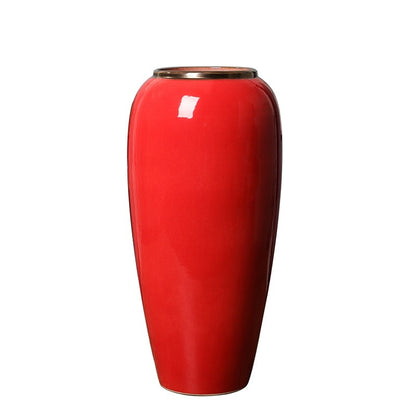 A glossy red ceramic vase with a flared rim and a small metallic gold accent at the top, shown against a plain white background.
