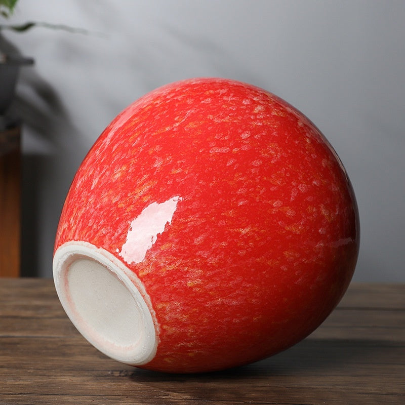 A glossy ceramic bowl with a vibrant red glaze and subtle gold speckling, shown on a dark wooden surface against a soft gray background.